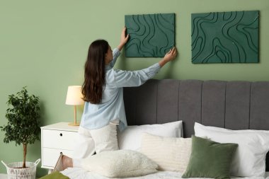 Yatak odasındaki yeşil duvara resim asan genç bir kadın. Arka plan