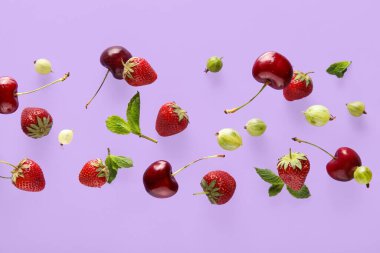 Farklı çilekler ve nane yaprakları eflatun arka planda uçuşuyor, yakın plan