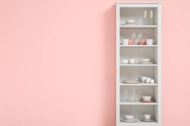 Mutfakta pembe duvarın yanında tabakları olan modern raf ünitesi.