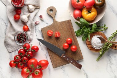 Domatesler, bıçaklı kesme tahtası, fesleğen ve beyaz arka planda sarımsak. Üst görünüm