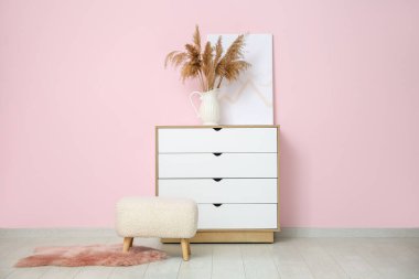 Çekmeceler, otlar, resim ve pouf pembe duvarın yanında.