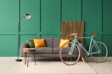 Rahat kanepe, ekran, lamba, sehpa ve bisiklet oturma odasında yeşil duvarın yanında.