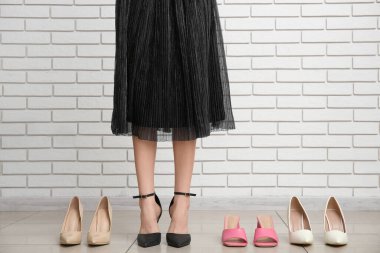 Ayak bileği bağcıklı genç bir kadın diğer ayakkabılar arasında beyaz tuğla duvara yaslanmış.