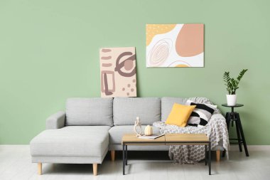 Yeşil duvarda asılı resim, rahat bir kanepe, sehpa ve odadaki çiçek.