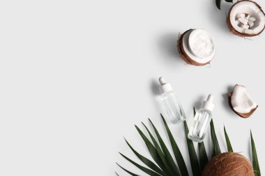 Hindistan cevizi kozmetik yağı ve gri arka planda palmiye yaprağı olan bir kase krema.