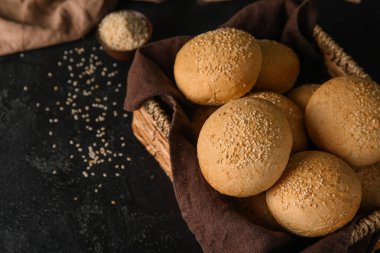 Siyah zemin üzerinde susam tohumları olan bir sepet taze çörek.