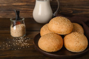 Susam tohumlu taze çörekler ve tahta arka planda bir sürahi süt.