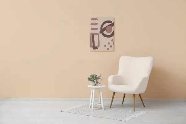 Painting hanging on beige wall and armchair with houseplant in room
