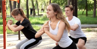 Spor yapan genç insanlar dışarıda çömeliyor.