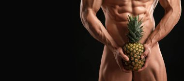 Karanlık arka planda ananas tutan seksi çıplak vücut geliştirici. Mesaj için yer var, yakın plan.