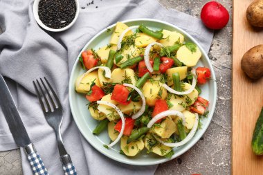 Bir tabak lezzetli patates salatası, sebze ve arkaplanda malzemeler var.