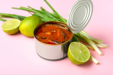 Domates soslu balıklı konserve kutusu, pembe arka planda limon ve soğan.