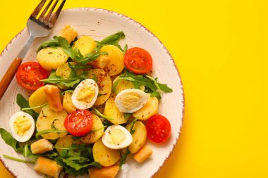 Sarı arka planda yumurta ve domatesli lezzetli patates salatası.