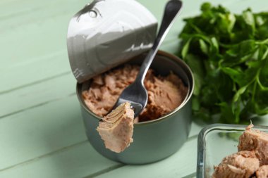 Lezzetli ton balığı ve çatallı konserve kutusu yeşil ahşap masada, yakın plan.