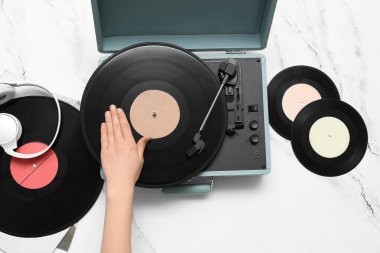 Beyaz arka planda vinil diskleri ve pikabı olan bir kadın.