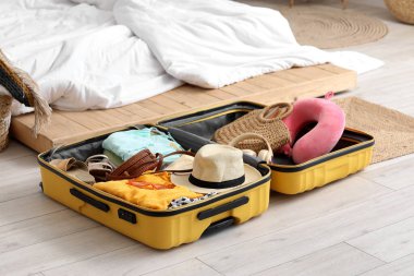 Yatak odasında yerde plaj aksesuarlarıyla dolu bavulu aç.