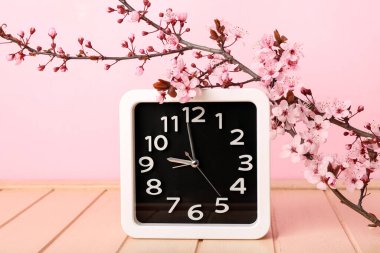 Çiçekli bahar dalları ve pembe ahşap masadaki saat