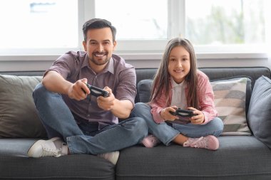 Babası ve küçük kızı evde video oyunu oynuyorlar.