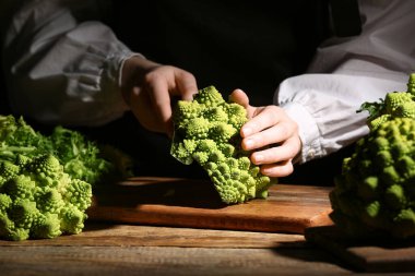 Romanesco brokolisini koyu arka planda kesen kadın, yakın plan.