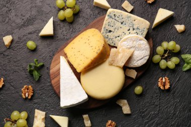 Tahta tahta tahta tahta, farklı çeşitlerde lezzetli peynir, fındık ve üzümler koyu arka planda.