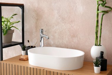 Masada bambu saplı lavabo, banyo aksesuarları ve vazo var.