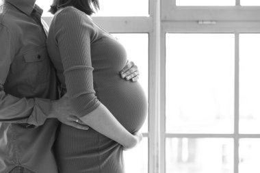 Evde pencerenin yanında genç hamile bir çift sarılıyor.