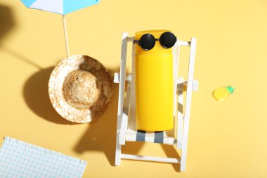 Güneş gözlüklü güneş kremi ve soluk sarı arka planda plaj aksesuarlarıyla yaratıcı kompozisyon.