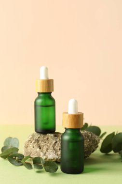 Okaliptüs dalları ve yeşil masa üzerinde taş olan kozmetik yağları.