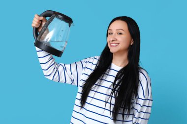 Mavi arka planda modern elektrikli su ısıtıcısı olan güzel genç bir kadın.