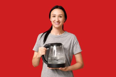 Kırmızı arka planda modern elektrikli su ısıtıcısı olan güzel genç bir kadın.