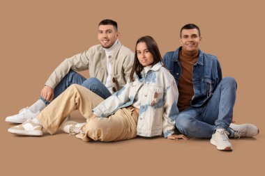 Kahverengi arka planda oturan kot elbiseli şık genç insanlar.