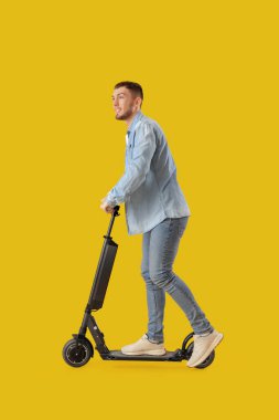 Sarı arka planda elektrikli scooter kullanan genç adam.