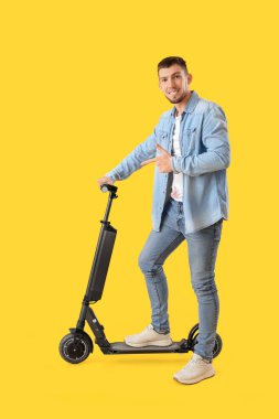 Sarı arka planda elektrikli scooter 'ı gösteren genç adam.
