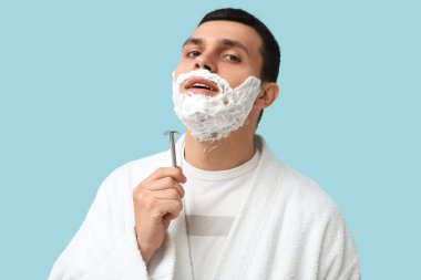 Yüzünde jilet ve tıraş köpüğü olan yakışıklı genç bir adam.