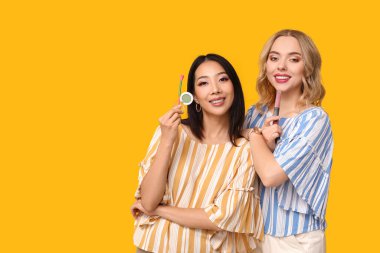 Sarı arka planda dekoratif kozmetik ürünleri olan güzel genç kadınlar.