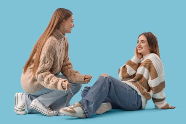 Genç lezbiyen kadın mavi arka planda kız arkadaşının ayakkabı bağcıklarını bağlıyor.