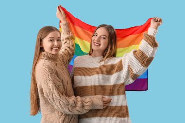 Mavi arka planda LGBT bayrağı olan sıcak kazaklı genç lezbiyen çift