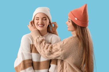 Mavi arka planda sıcak şapkalar takan genç lezbiyen çift