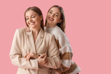 Genç lezbiyen çift pembe arka planda sarılıyor.