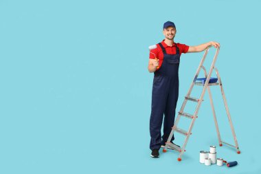 Mavi arka planda boya silindiri ve merdiveni olan erkek ressamın portresi