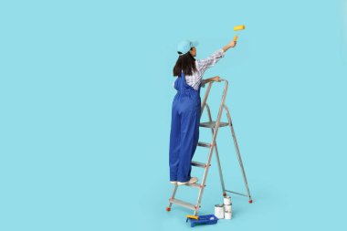 Mavi arka planda boya kutuları, tepsileri ve merdiveni olan Asyalı kadın ressam