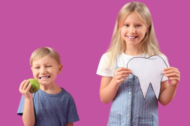 Kağıt dişi ve mor arka planda taze elması olan şirin, mutlu çocuklar.