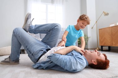 Küçük çocuk evde babasını gıdıklıyor.