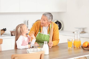 Sevimli küçük kız ve mutfak masasında mutfak aletleri pişiren büyükannesi.