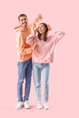 Pembe arka planda sıradan giyinmiş mutlu genç çift.