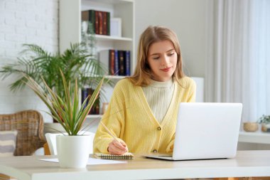 Ofisteki masada dizüstü bilgisayarı ve defteri olan kadın yazar
