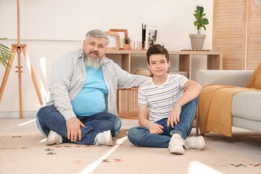 Mutlu büyükbaba ve tatlı torunu evde yerde oturuyor.