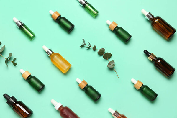 Бутылки косметического масла и эвкалиптовые ветви на бирюзовом фоне