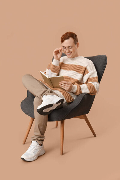 Молодой человек сидит на кресле и читает книгу на цветном фоне