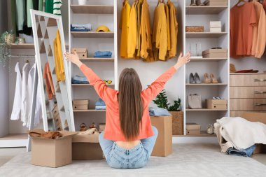 Giysi kutuları ve şık elbiseleri olan güzel genç bir kadın soyunma odasında oturuyor.